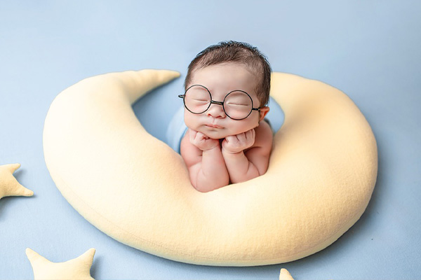 baby with glasses laying on a moon-shaped pillow